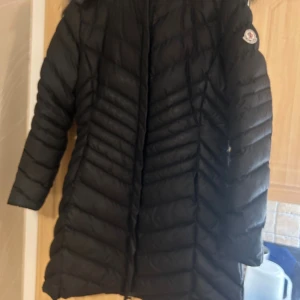 Svart Moncler dunjacka med päls - Säljer en svart lång dunjacka från Moncler ni som vet ni vet. med snyggt mönstrad vaddering och huva med fluffig päls. Jackan har dragkedja framtill och Moncler-logga på ärmen. Perfekt för kalla dagar och riktigt stilren look. Köpte den på vinted,har aldrig använt den då den va för liten för mig. Det står XXL men är nog mer än M L. Priset är inte hugget i sten och går och förhandla. 