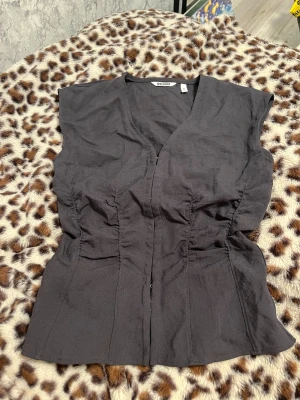 Svart korsettopp från Weekday, strl 36 - Säljer en svart korsettopp från Weekday i storlek 36. Toppen har v-ringning, croppad passform och snygga rynkade detaljer på sidorna. Stängs med hakar framtill och är ärmlös. Materialet är linneblandning som ger en cool och stilren look.