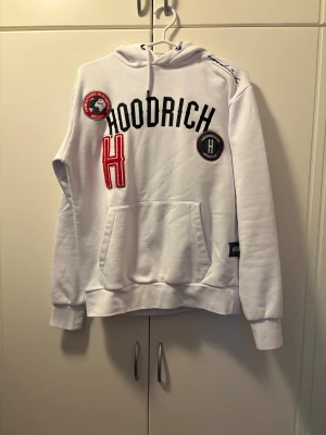 Vit hoodie från Hoodrich XS - Säljer en vit hoodie från Hoodrich i storlek XS. Tröjan har broderade patches och text på framsidan, snörning vid huvan och en stor magficka. Hoodien har långa ärmar och coola detaljer som sticker ut. Perfekt för dig som gillar streetwear och vill ha något unikt. Det ända felet på den det är att h ett den ha låsbar lite tror man ser det på bilden 