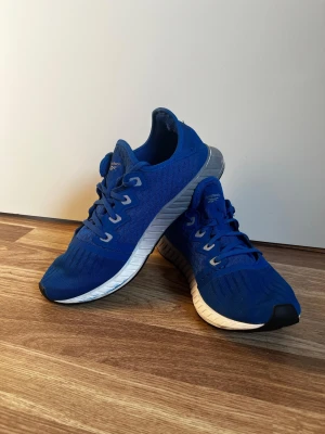 Blå Reebok sneakers med mesh - Säljer ett par blå Reebok sneakers med vit och grå sula. Skorna har snörning, rund tå och är tillverkade i mesh och syntetmaterial för en sportig look. Perfekta för dig som gillar stilrena träningsskor med cool design.