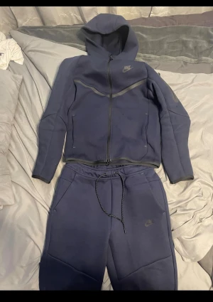 Marinblå Nike hoodie med dragkedja - Säljer en marinblå hoodie från Nike med hel dragkedja och huva. Tröjan har snygga detaljer i mörkgrått och Nike-logga på bröstet. Perfekt för chill eller träning, med mjukt material och sportig look.