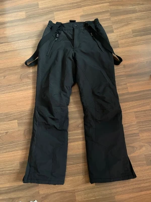 Termobyxor/skidbyxor med hängslen  - Svarta termobyxor från etirel. Passar bra till vintern och skidåkning. Avtagbara hängslen och fickor med dragkedja. Mycket fint skick