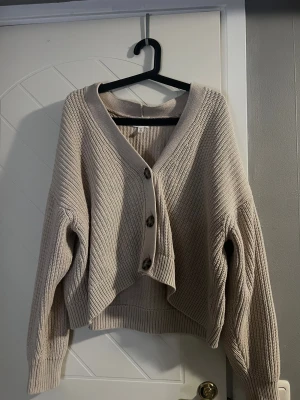 Beige stickad kofta med knappar - Säljer en beige stickad kofta, den är v-ringad med tre knappr. Koftan har en loose passform och långa ärmar
