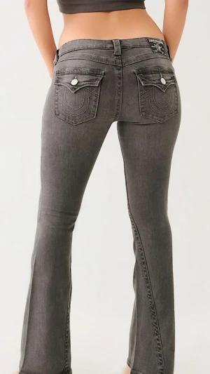 Grå bootcut jeans från True Religion Becca - Snygga grå jeans från True Religion med bootcut passform. Jeansen har dekorativa bakfickor med lock och silverfärgade knappar samt tydliga sömmar. Klassisk femficksmodell i stretchigt denimtyg som sitter tajt upptill och släpper vid benslutet.