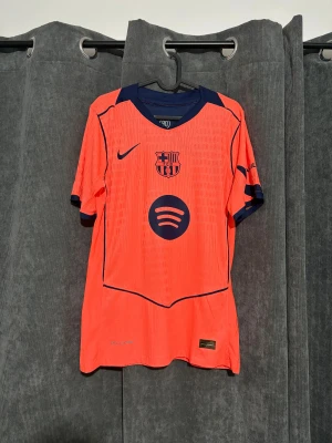 FC Barcelona Pedri #8 Nike fotbollströja, Size S/M - Snygg FC Barcelona matchtröja med Pedri #8 på ryggen. Tröjan är orange med marinblå detaljer, klubbmärke och Nike-logga på bröstet samt Spotify och UNHCR tryck. Tillverkad i lätt, ventilerande polyester med korta ärmar och modern passform.