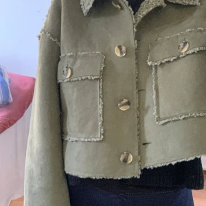 Grön croppad teddyjacka med fickor - Snygg croppad teddyjacka från Asos i olivgrönt med fluffig krage och detaljer längs kanterna. Jackan har två stora fickor framtill och coola knappar. Perfekt för dig som gillar streetstyle och vill sticka ut lite extra. Är i storlek xl men passar bra på mig i storlek s/m