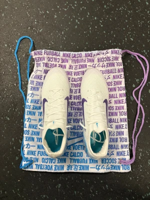 Nike Mercurial vapor 16 chromatic - Nike Mercurial fotbollsskor i vit med lila swoosh och blå detaljer. Skorna har snörning, spetsig tå och en platt sula med blå och lila mönstrad undersida. Ovandelen är i syntetmaterial för lätt vikt och bra grepp på planen. Perfekt för dig som vill sticka ut med stil på fotbollsplanen. Size 40 fits 40.5, used once, limited edition