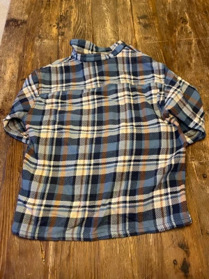 Blå och brun rutig skjorta med knappar - Snygg rutig skjorta i blått, brunt och vitt med klassisk krage och tryckknappar framtill. Lite tjockare skjorta. Skjortan har två bröstfickor med lock och långa ärmar. 