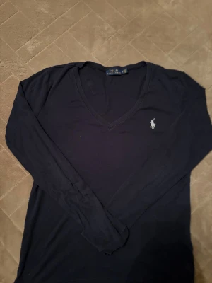 Marinblå långärmad tröja Polo Ralph Lauren - Snygg marinblå långärmad tröja från Polo Ralph Lauren med klassisk v-ringning och vit broderad logga på bröstet. Tillverkad i mjuk bomull som känns skön mot huden. Perfekt för dig som gillar stilrena och tidlösa plagg. Bra julklapp till en tjej ❤️🔥om det syns några fleckar så är det sånt som går att tvätta 🧽 🔥