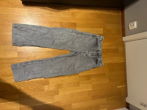 Grå wide jeans från Never Denim - Snygga grå jeans från Never Denim med breda ben och klassisk femficksdesign. Jeansen har en ljusgrå tvätt och är tillverkade i jeansmaterial. Passformen är wide och midjan är normal. Perfekta för dig som gillar en avslappnad stil. OBS: Dessa jeans är uppsydda för att passa mig (180) men om man tar bort uppsyningen så passar de 195 ungefär.