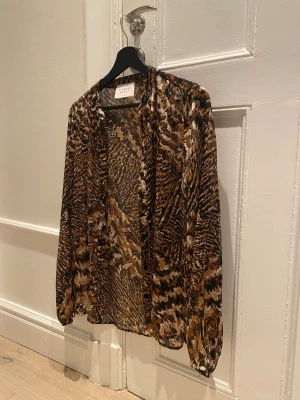 Leopardmönstrad skjorta Sisters Point - Tunn/transparent kofta/blus med leopardmönster i bruna, svarta och beige toner. Ärm med lätt puff och elastisk mudd vid ärmslut. Går att stänga med knappar framtill☺️