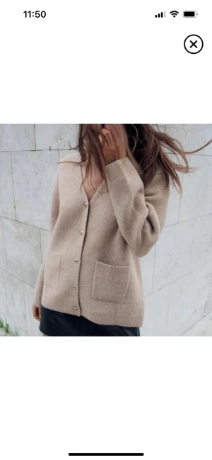 Zara Beige kofta med fickor och guld knappar - Supermjuk beige kofta med v-ringning, stora framfickor och snygga guldfärgade knappar. Koftan är lite oversized och har långa ärmar, perfekt att slänga på sig över en topp. Materialet ser ut att vara stickat och ger en chill och stilren vibe.