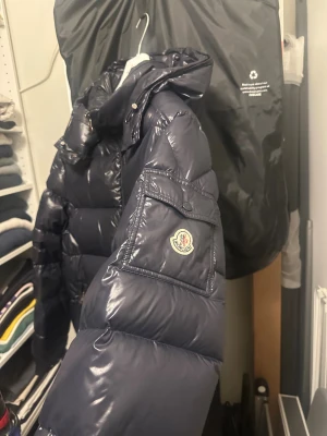 Moncler Maya - Hej, säljer min Moncl3r Maya i mörkblå.   Skick: 8/10, små flaws, men annars fin. Cartoon har lossnat men ska tydligen vara rätt vanligt för modellen. Cartoon har jag sparat så skulle man vilja sätta tillbaka den så följer den med. Storlek: 7  Nyligen vart på kemtvätt.   Köpt på NK Stockholm så har kvitto, prislapp och extra knappar och resterande som medföljde vid köp.   Bin: 6000kr men tar emot bud.   Köparen står för frakten om man ej kan mötas upp i Stockholm  Skicka iväg ett PM vid ev frågo