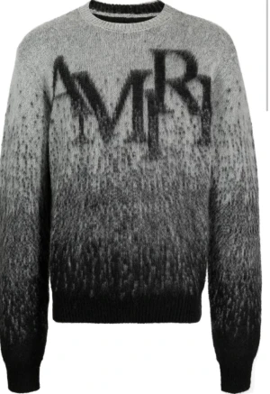 Grå stickad tröja från AMIRI - Snygg stickad tröja från AMIRI i grå och svart ton med stor logotyp framtill. Köpte den nere i Italien och har tyvärr tappat bort kvittot och vet att den går ner i värde då fast är öppen till en konversation om att sänka priset 
