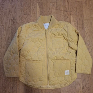 Gul quiltad bomberjacka Minimarket - Quiltad bomberjacka från Minimarket i ljusgul färg. Jackan har ribbad krage, dragkedja framtill och tre praktiska fickor. Materialet är mjukt och lätt, perfekt för vår och höst. Snyggt mönstrad med rundade quiltade sömmar för extra stil.