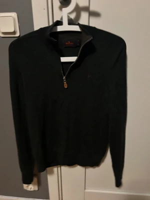 Svart half zip stickad tröja Morris - Svart stickad tröja från Morris med half zip och lång ärm. Tröjan är Storlek S och har en liten defekt vid halsen men den syns knappt annars är skicket bra. Hör av dig vid minsta fundering 