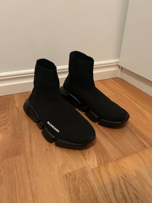 Svarta Skor - sneakers med stickad ovandel och chunky platt sula. Snygg minimalistisk design med b-logga på sidan. Strumpliknande passform och rund tå. Perfekt för dig som gillar streetstyle och vill ha något unikt på fötterna.