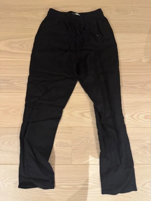 Svarta linnebyxor från Les Deux - Svarta linnebyxor från Les Deux med elastisk midja och snörning. Byxorna har en rak passform och sidofickor fram samt bakfickor. Perfekta för en chill och stilren look, tillverkade i mjukt linne som ger en skön känsla.