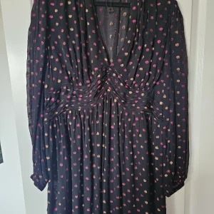 Svart långklänning med prickar Indiska - Svart klänning från Indiska i storlek XL med glittriga prickar i rosa och guld. Klänningen har v-ringad hals, långa ärmar och ett snyggt rynkat midjeparti som ger en cool siluett. Perfekt för dig som gillar att sticka ut med färg och glitter.