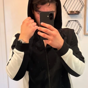 Svartvit hoodie från BOSS - Säljer en svart hoodie från BOSS med vita paneler längs ärmarna och axlarna. Tröjan har dragkedja hela vägen, huva och BOSS-logga på kragen. Perfekt för dig som gillar sportig och stilren look. Original pris 1080. Pris går att diskuteras.