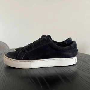 Marin blå mockasneakers från Vagabond - Stilrena sneakers från Vagabond i mjuk mocka med vit platt sula. Klassisk låg modell med rund tå och snörning framtill. Perfekta för dig som gillar minimalistisk och clean stil. Diskret Vagabond-logga bak på sulan. Passar 42-43