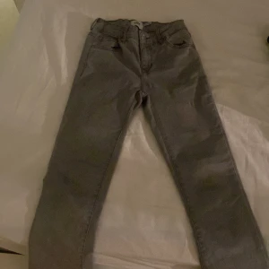 Grå jeansbyxor i rak modell - Snygga grå jeansbyxor med klassisk femficksdesign och rak passform. Byxorna har bälteshällor, dragkedja och knapp framtill. Perfekta för dig som gillar en enkel och stilren look. Passar till det mesta och är lätta att matcha med olika outfits.