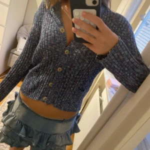 Blåmelerad ribbad kofta med knappar och framfickor  - Superfin blåmelerad kofta med ribbad struktur och snygga knappar framtill. Den har små framfickor som en snygg detalj. Färgen är en mix av blått, lila och lite vitt för en cool vibe. Ingen lapp eller märke tyvärr