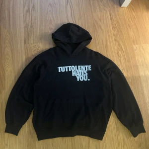  Tuttolente Hates You hoodie - Svart hoodie från Tuttolente med vit text 'TUTTOLENTE HATES YOU.' på bröstet. Stor luva och långa ärmar. Perfekt för dig som gillar streetwear och vill ha en statementtröja. Oversized fit, Aldrig använd endast provad!