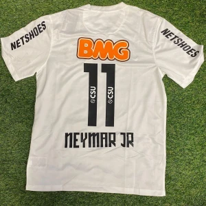 Vit Neymar Jr fotbollströja Santos - Snygg vit fotbollströja från Santos FC med Neymar Jr och nummer 11 på ryggen. Tröjan har korta ärmar, tryckta sponsorer och är tillverkad i lätt och ventilerande material. Perfekt för dig som vill sticka ut på planen eller visa support för Neymar.