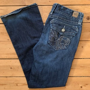 Mörkblå jeans från Madison med broderi W34 L32 - Mörkblå jeans från Madison med snygga broderade bakfickor och dekorativa knappar. Klassisk femficksmodell med dragkedja och knapp framtill. Jeansen har raka ben och är tillverkade i stretchigt denim för extra komfort.   Storlek W34 L32