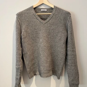 Grå stickad tröja från J.Lindeberg - Säljer en grå stickad tröja från J.Lindeberg med v-ringad hals och ribbade muddar. Tröjan har en klassisk passform och är perfekt för lager-på-lager under kyliga dagar. Enkel och stilren design som funkar till det mesta. Tröjan är storlek L men passar M. Priset är inte spikat så hör av er