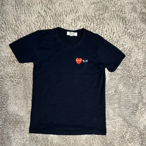 Cdg T-shirt  - Mörkblå  t-shirt från Comme des Garçons Play med två broderade hjärtan på bröstet, ett rött och ett mörkblått. Klassisk passform med rund hals och korta ärmar. Tillverkad i mjuk bomull för en skön känsla.