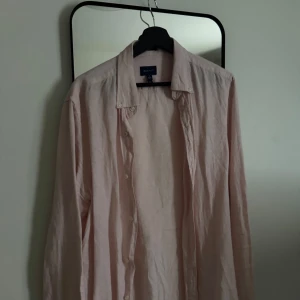 Ljusrosa linneskjorta från Gant - Säljer en stilren ljusrosa skjorta från Gant i luftigt linne. Skjortan har klassisk krage, knäppning framtill och långa ärmar. Perfekt för en avslappnad men ändå snygg look.