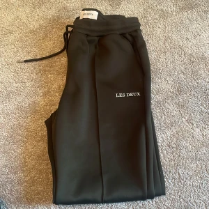 olivgröna mjukisbyxor från Les Deux - Olivgröna mjukisbyxor från Les Deux med raka ben och snörning i midjan. Byxorna har en stilren look med diskret logga på låret och sydda pressveck framtill. Perfekta för en chill och snygg stil.