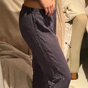 Randiga byxor från Holly & Whyte - Mörkblå byxor med vita tunna ränder från Holly & Whyte by Lindex. De har elastisk midja och är raka i modellen, vilket gör dem riktigt sköna och avslappnade. Perfekta för dig som gillar en chill och stilren look. Fungerar även utmärkt som pyjamasbyxor.