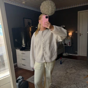 Vit fleecekofta med knappar - Mysig vit fleecekofta med rund hals och tryckknappar framtill. Koftan har en oversized passform och är tillverkad i fluffigt fleecematerial. Perfekt för kyliga dagar och enkel att styla till olika outfits.