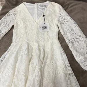 Vit spetsklänning från Dry Lake - Superfin vit kortklänning från Dry Lake i spets med blommigt mönster. Klänningen har v-ringning, långärmade ärmar och dragkedja i ryggen. Den är helt ny med prislappen kvar!!