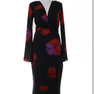 Svart långklänning med blommor från Adoore - Supersnygg svart långklänning från Adoore med stora röda och lila blommor, v-ringning och lång ärm. Klänningen har en slits framtill och markerad midja som ger en riktigt elegant siluett. Perfekt för dig som vill sticka ut med stil.