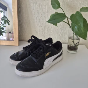 Svarta Puma sneakers - Snygga svarta sneakers från Puma med klassisk vit sidodetalj och guldfärgad logga. Använda en del men i fint skick! Slitna i hälarna men annars bra! Personligen tycker jag inte att slitaget i hälarna känns när man använder skorna🤍