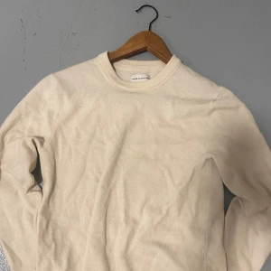 Beige merinoulltröja These Glory Days - Säljer en stilren beige tröja från These Glory Days i mjuk och lyxig merinoull. Tröjan har rund halsringning och långa ärmar, perfekt för lager-på-lager under kyliga dagar. Enkel design som funkar till allt och ger en clean look.