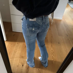 True Religion ljusblå bootcut jeans - Säljer ett par ljusblå jeans från True Religion. Jeansen har låg midja och bootcut passform, tillverkade i klassiskt denim med snygg tvätt och detaljerad brodyr på fickorna. Nypris 1599. Har använt byxorna endast 3 gånger då jag snabbt märkte att jag köpt fel storlek. Midjestorleken är 27, och längden 34.