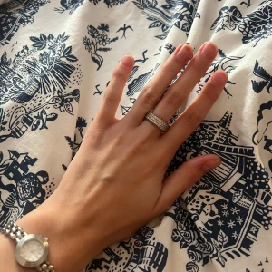 Glittrig silverring från Pandora - Säljer en snygg och glittrig silverring från Pandora i storlek 52. Ringen är täckt med små gnistrande stenar runt hela och har en bred, rund form som verkligen syns på handen. Perfekt för dig som gillar bling och vill sticka ut lite extra. (Originalpris 1499kr)