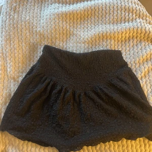 Svart kortkjol från Gina Tricot XS - En svart kortkjol från Gina Tricot i storlek XS. Kjolen har en fluffig, strukturerad yta och är lätt utställd med markerad midja. Perfekt för dig som vill ha en enkel men ändå unik kjol i garderoben.