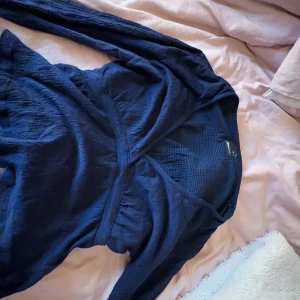 Mörkblå omlottopp från Gina - Säljer en mörkblå omlottopp från gina med lång ärm och v-ringning. Perfekt att styla med jeans eller kjol.