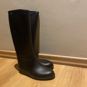 Svarta ridstövlar från ELT, stl 36 - Säljer ett par klassiska svarta ridstövlar från ELT i storlek 36. De är höga med platt sula och rund tå, tillverkade i syntetmaterial. Perfekta för dig som vill ha en stilren look i stallet. Det är en liten klack så man inte tappar stigbygeln men den passar perfekt för dig som vill ha en bekväm sko. Några repor vid tån men inget man märker när man har de på sig 