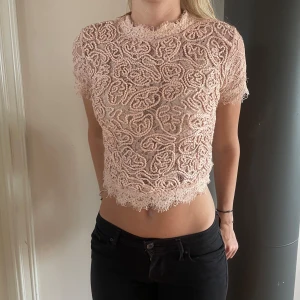 Zara ljusrosa spetsig croppad blus - Säljer en ljusrosa croppad blus med korta ärmar och hög hals. Toppen har ett unikt spetsmönster med broderade detaljer och fransig kant nertill och vid ärmslut. Perfekt för dig som gillar söt och trendig stil.