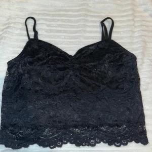 Svart spetsig linnetopp - Snygg svart linnetopp i spets med tunna axelband och v-ringad form. Toppen är croppad och har fina spetsdetaljer längs nederkanten.