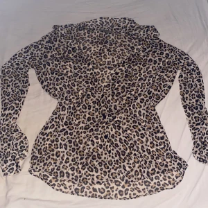 Leopardmönstrad skjorta med långa ärmar - Snygg transparent skjorta med leopardmönster och långa ärmar. Skjortan har klassisk krage och knäppning framtill, perfekt för dig som vill sticka ut med en trendig look.