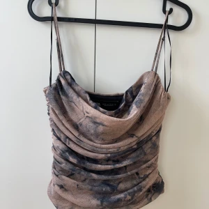 Beige och svart draperad linnetopp Zara - Säljer en snygg draperad linnetopp från Zara i beige och svart med coolt batikmönster. Toppen har tunna axelband och en lös, rynkad passform framtill som ger en trendig look. Perfekt att styla med jeans eller kjol för en chill vibe.