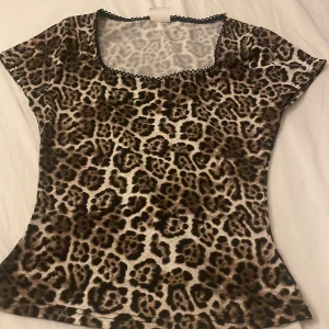 Leopardmönstrad topp från Stories XS - Snygg leopardmönstrad topp från Stories i storlek XS. Toppen har korta ärmar, rundad halsringning med svart spetskant och figurnära passform. Perfekt för dig som vill sticka ut med ett djurmönster och coola detaljer. Säljer då den inte kommit till användning ❤️